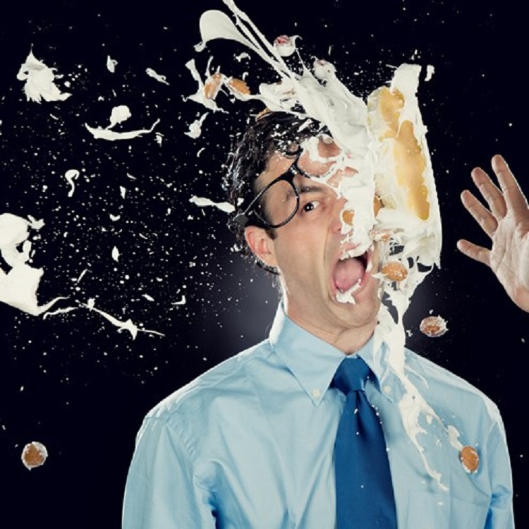Image of a grimacing man with pie being thrown on his face